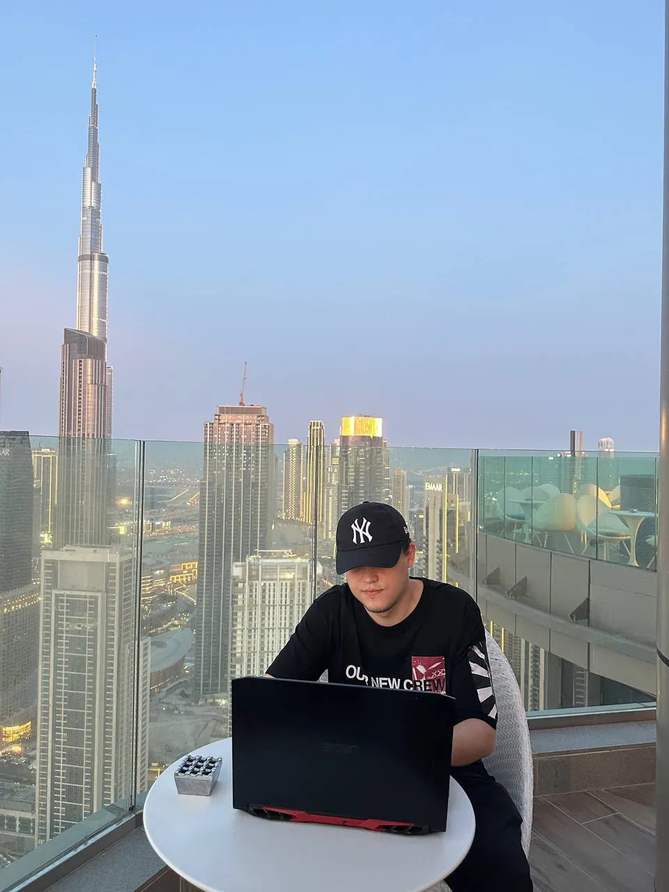Said at a laptop on a balcony in Downtown Dubai at dusk, the Burj Khalifa behind him